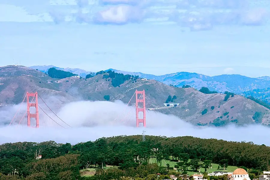 Birdseye view of Golden Gate Bridge towers above dense fog