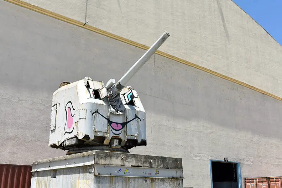 Abandoned naval gun with face painted on it in front of building
