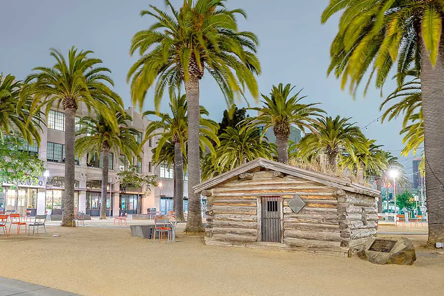 Log cabin in middle of square surrounded by palm trees