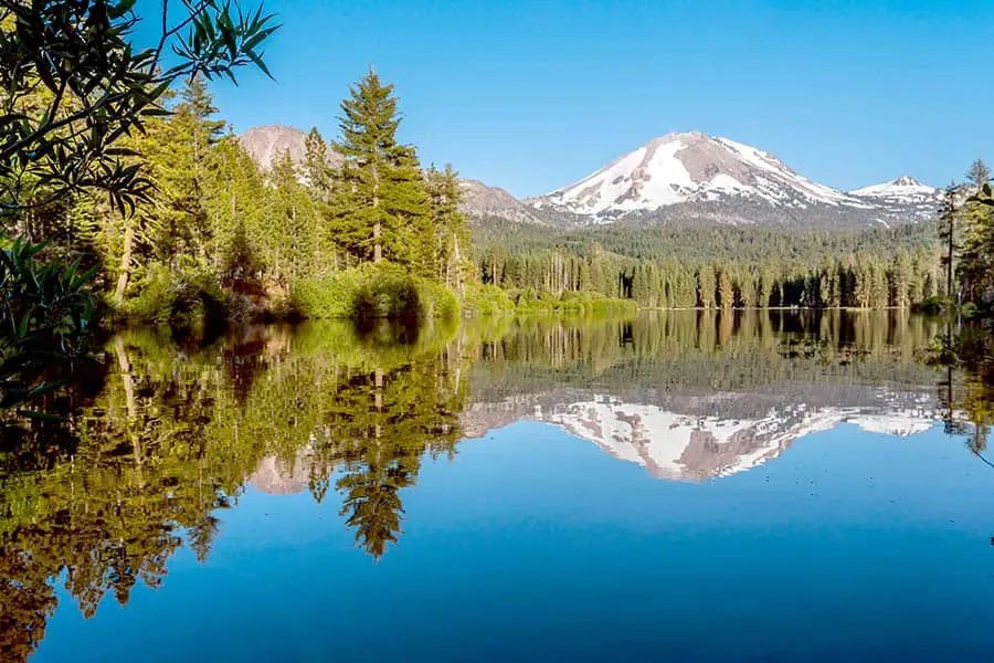 Lake surrounded by trees and snow capped Lassen Peak, California on horizon